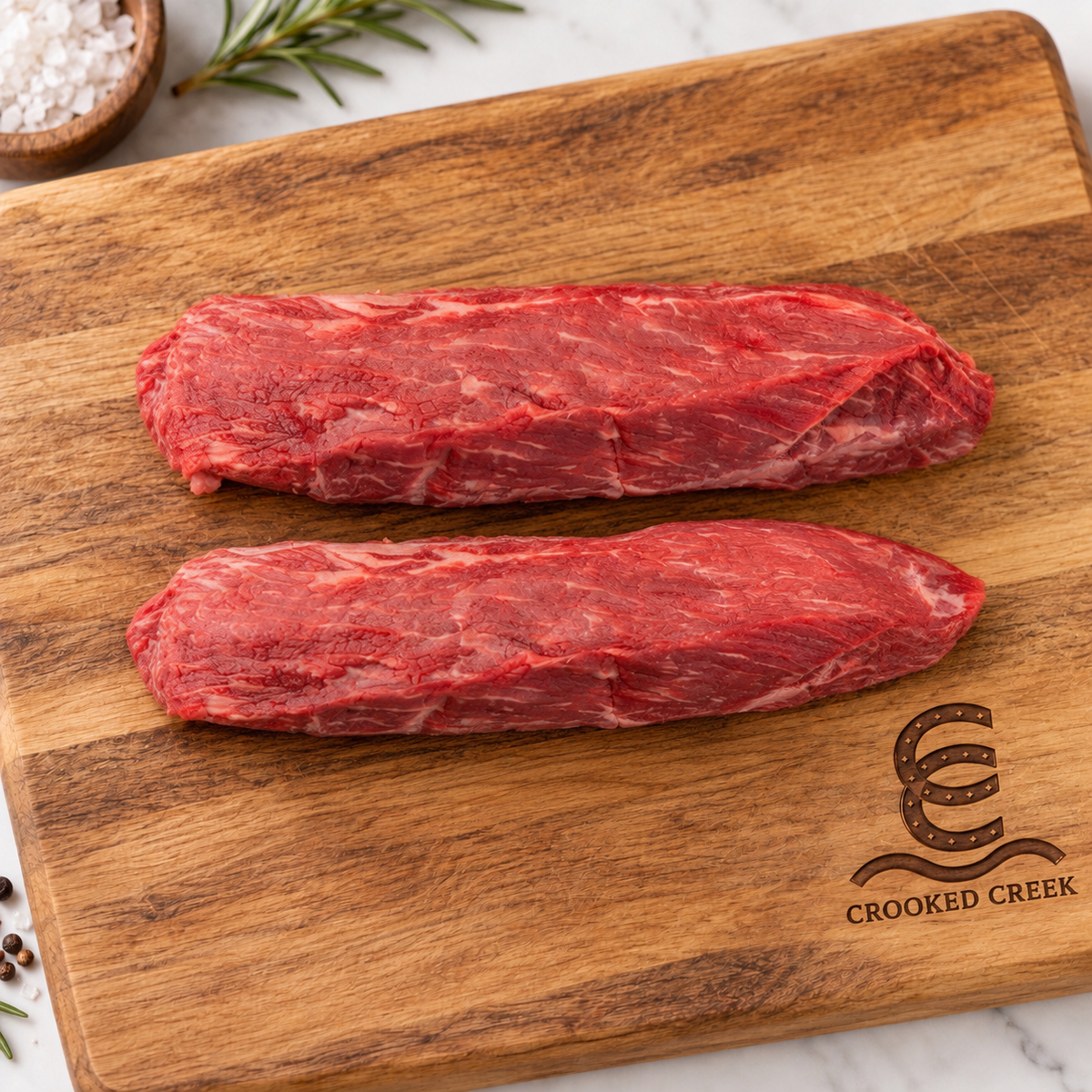 Two tapered tenderloin pieces on a Crooked Creek branded wooden cutting board